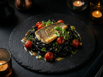 Wolfsbarschfilet
auf schwarzer Tintenpasta, geschwenkt
in Knoblauch-Weißweinbutter aus dem
Bratensatz, dazu gegrillte Kirschtomaten
Foto von Sascha Piontek Wolfsbarschfilet Seafood & Meer